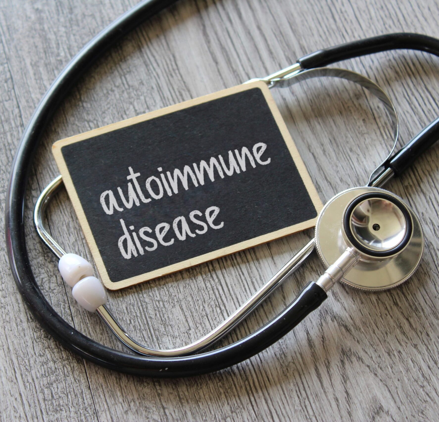 Stethoscope and chalkboard with text AUTOIMMUNE DISEASE on wooden table. Medical and healthcare concept